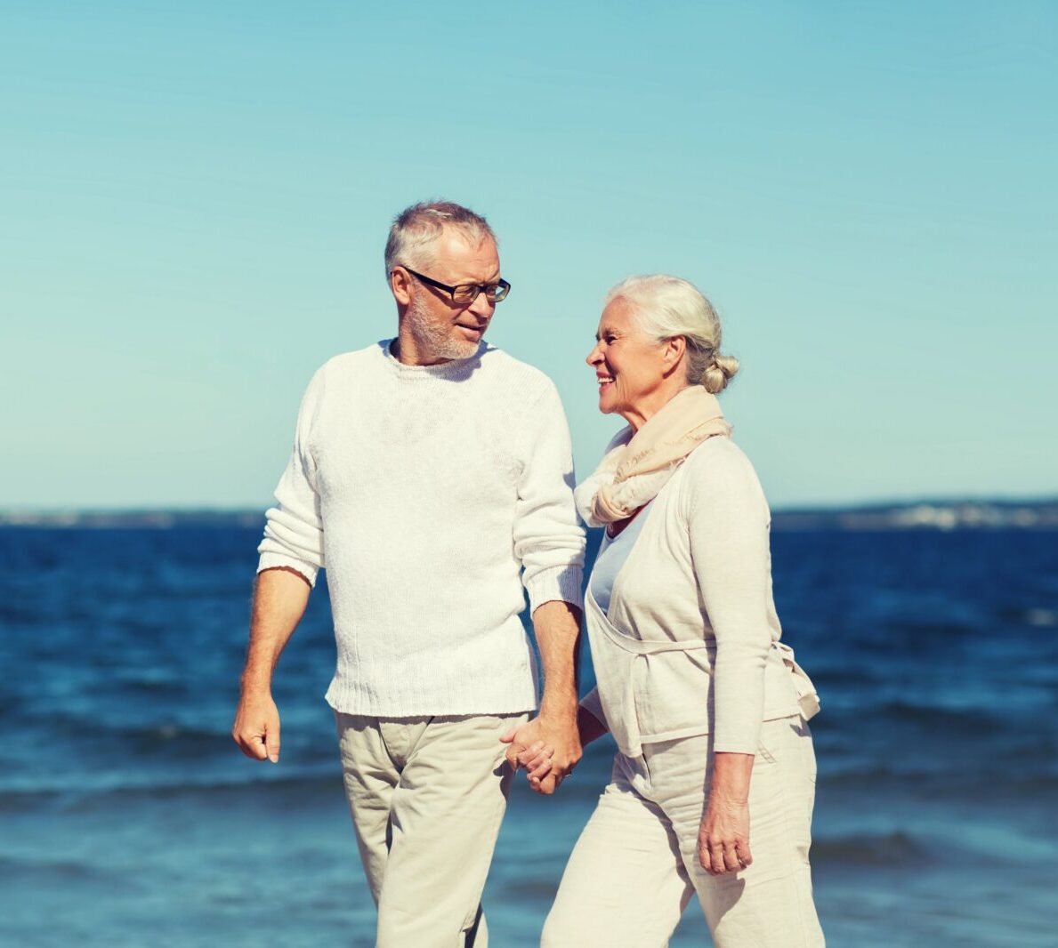 an elderly couple holding hands at the beach