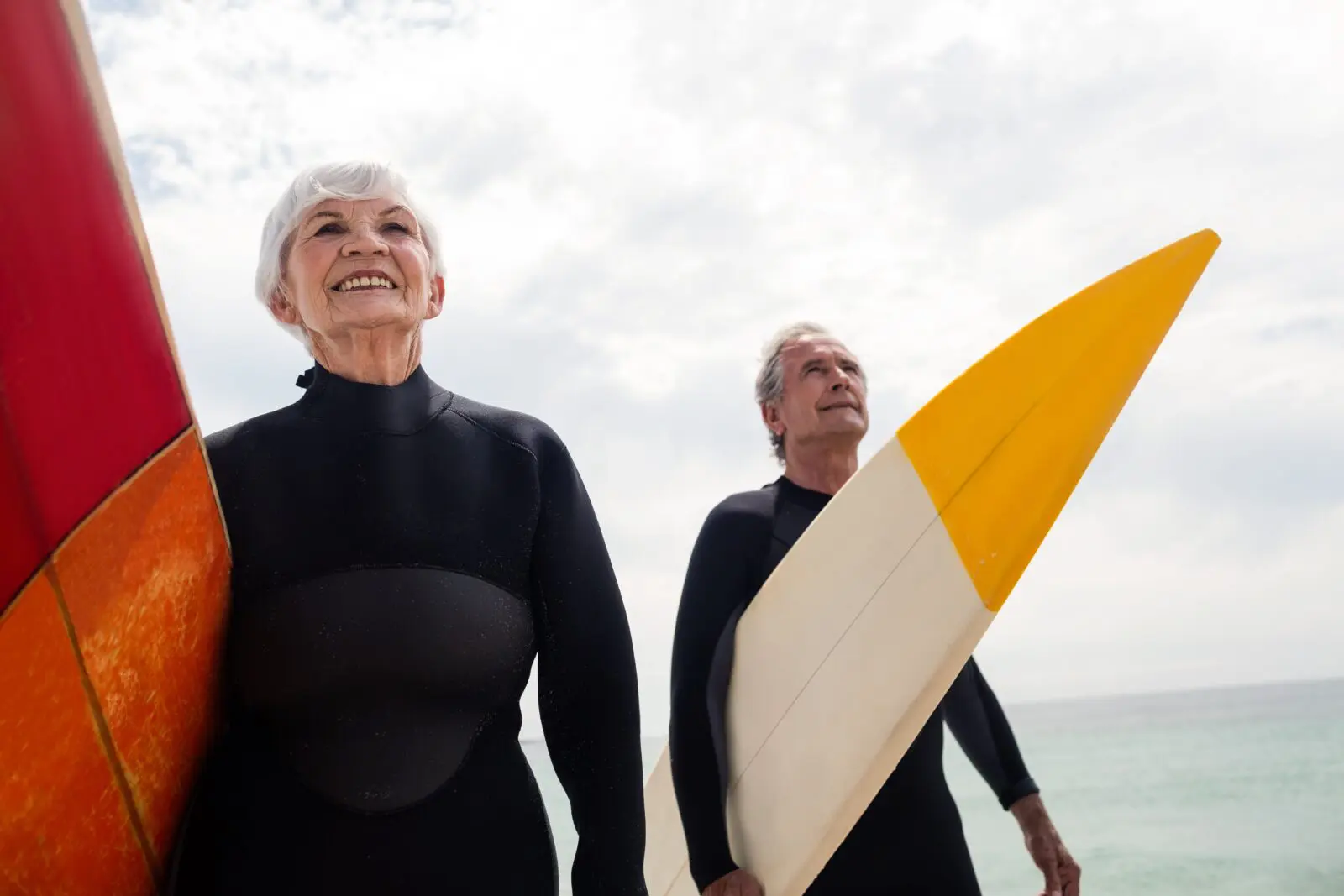 elderly couple holding surf boards