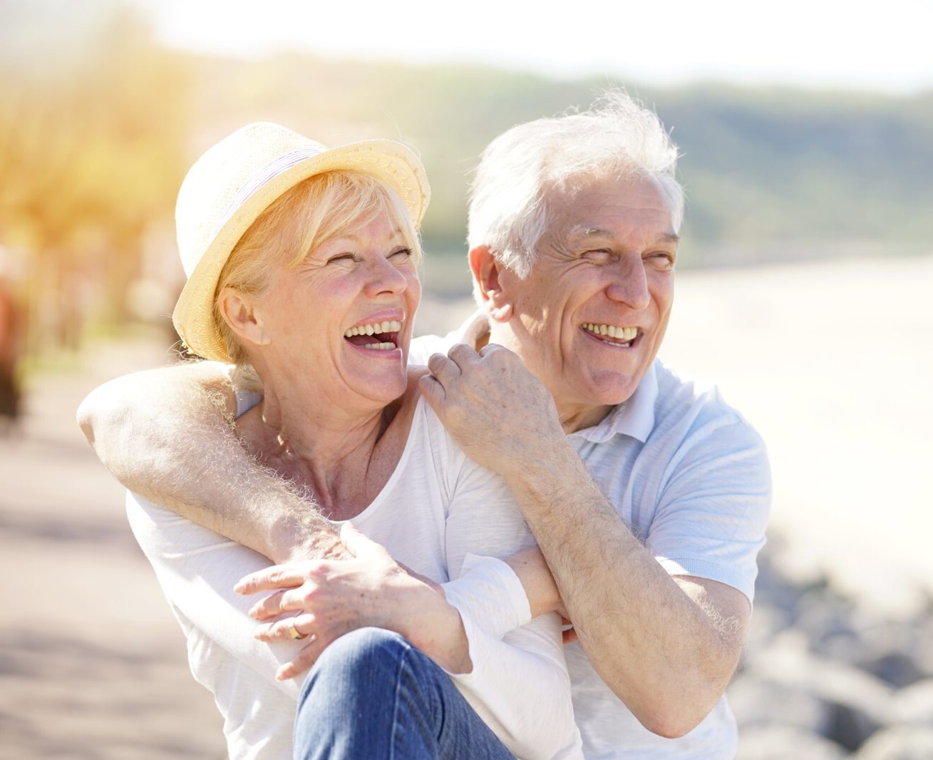 Laughing older couple embracing while sitting on a sunny beach